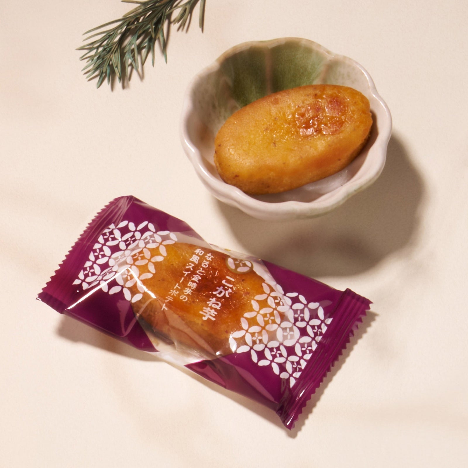 A wrapped and an unwrapped sweet from the Bokksu Snack Box: Seasons of Japan sit in a small ceramic dish on a light surface, with a pine branch nearby.