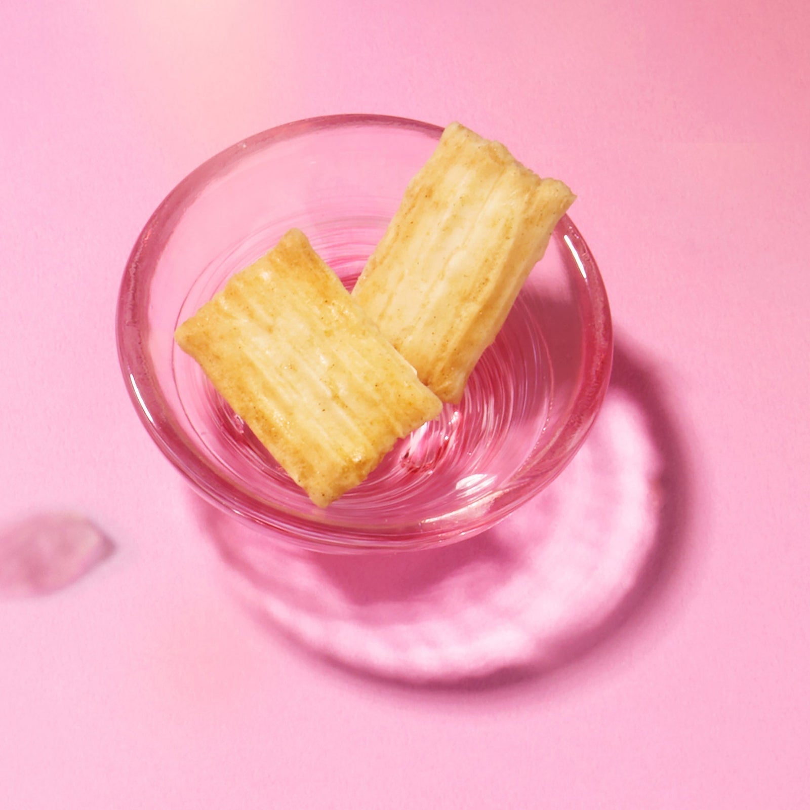 Two rectangular puff pastries in a clear pink glass bowl on a pink surface, evoking the refined Japanese treats found in the Bokksu Snack Box: Seasons of Japan.